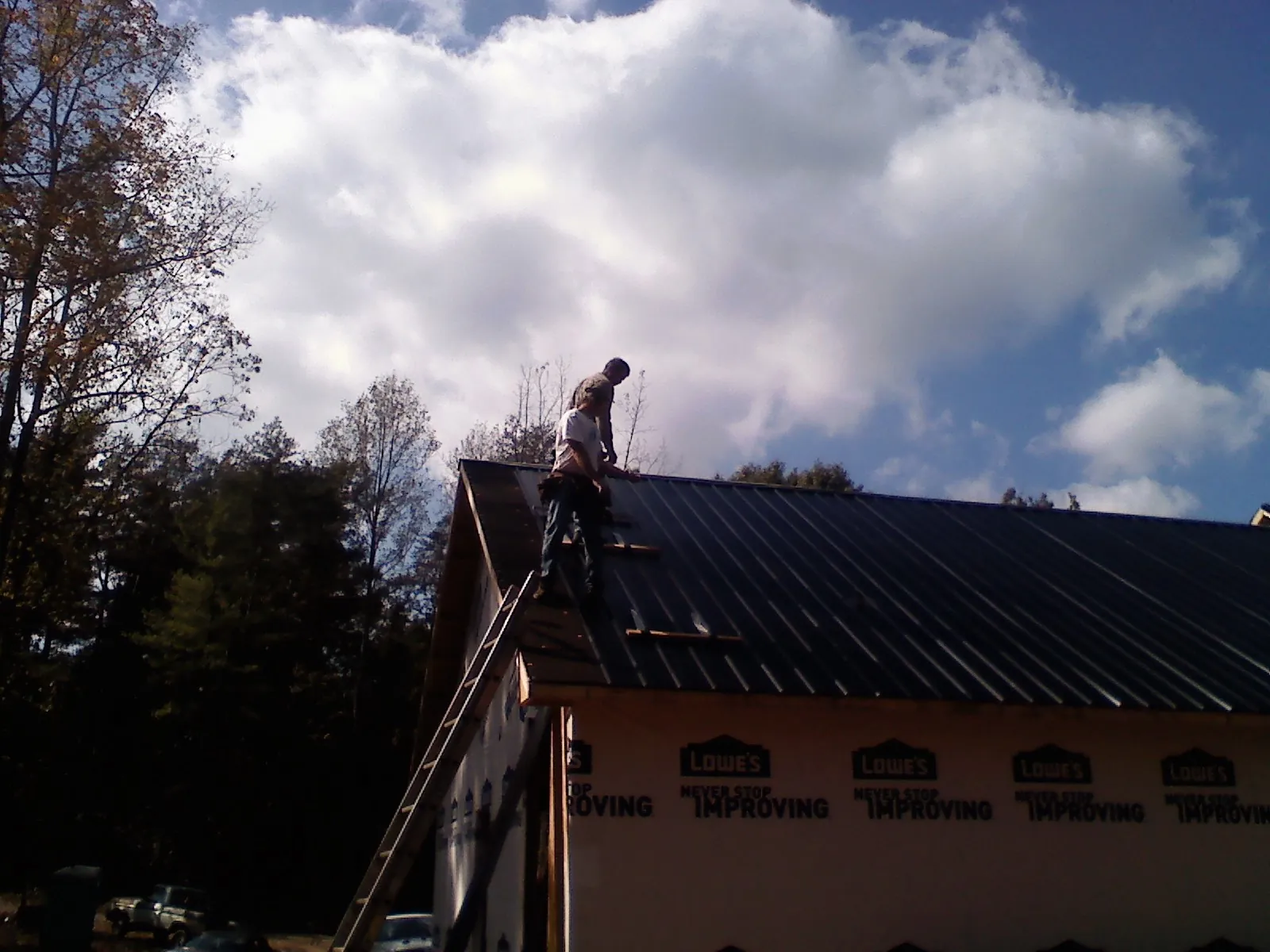 Roofer fastening dark metal panels high against a cloudy sky, from a Roof Inspection job in Veradale