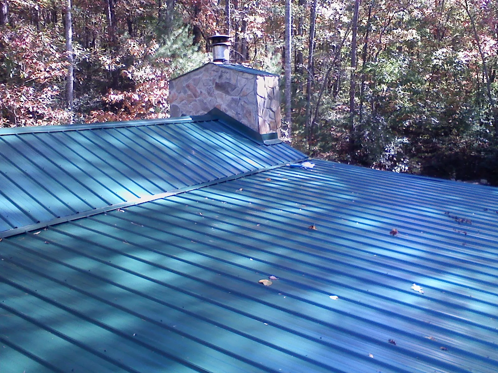 New green metal roof and stone chimney surrounded by autumn woods in Veradale