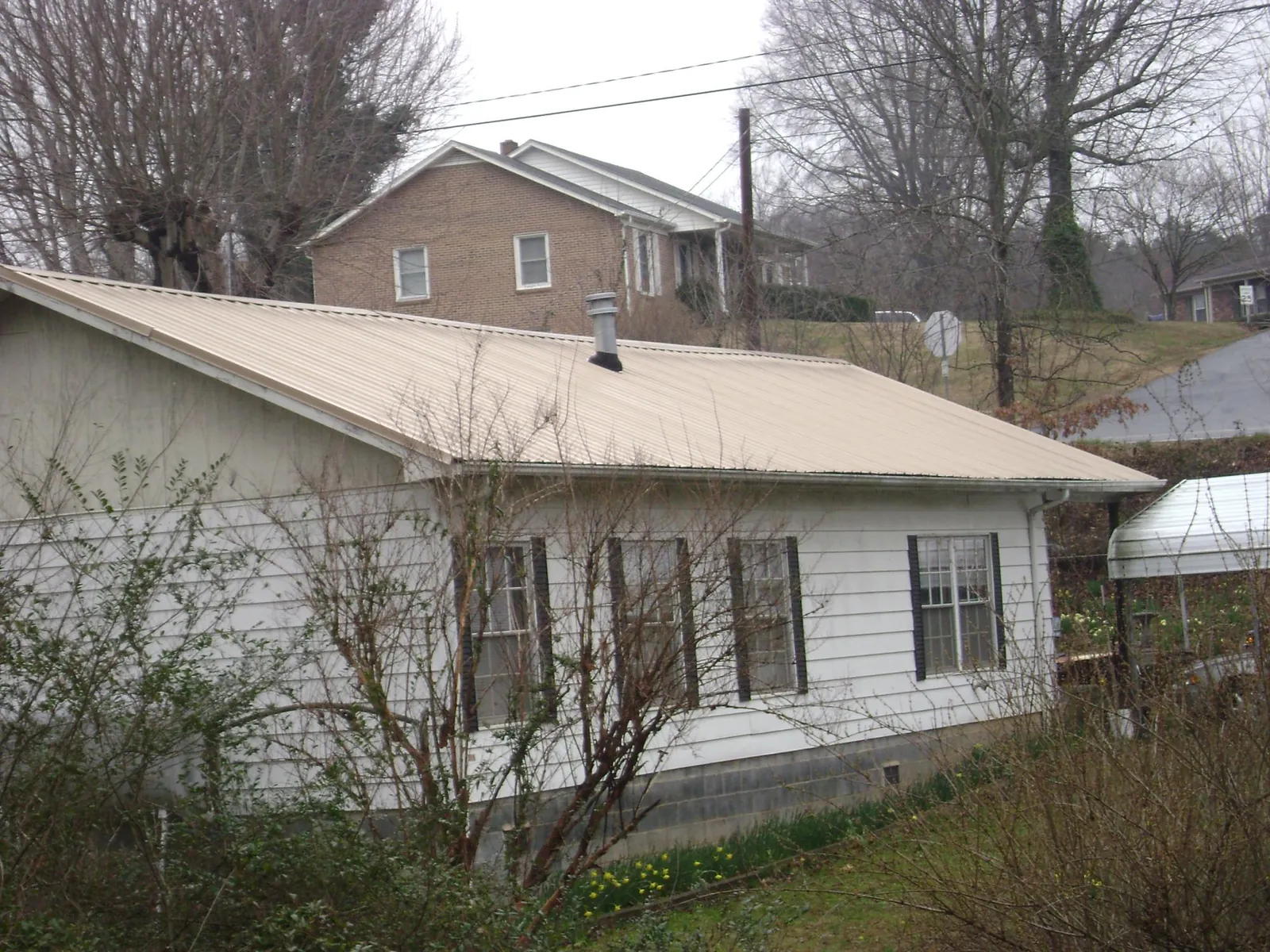 Tan metal roof on a white sided house set into a hillside — Commercial Roofing by Roofing Brothers in Veradale